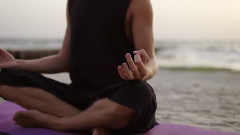 A-young-man-is-doing-yoga-and-meditating-on-a-sports-mat-while-sitting-during-the-dawn-of-the-sun.-Doing-a-specific-exercise.-Meditation,-hands.-Leisure-time,-recreation