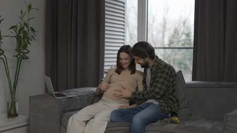 Pregnant-woman-with-large-belly-and-husband-sitting-on-sofa-waiting-for-movements