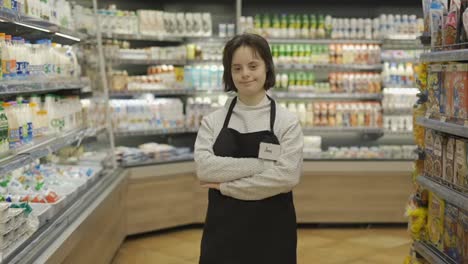 Portrait-of-a-shot-worker-with-Down-syndrome-standing-with-crossed-hands-at-supermarket
