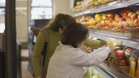 Down-syndrome-girl-with-her-mother-taking-vegetables-from-shelf-in-supermarket