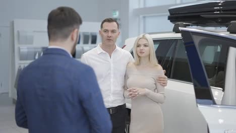 Portrait-couple-talking-to-car-dealer-in-dealership-discussing-the-chosen-car