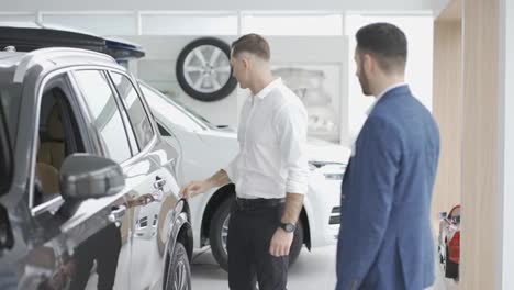 A-male-client-choosing-car-at-dealership-with-the-help-of-auto-seller,-slow-motion