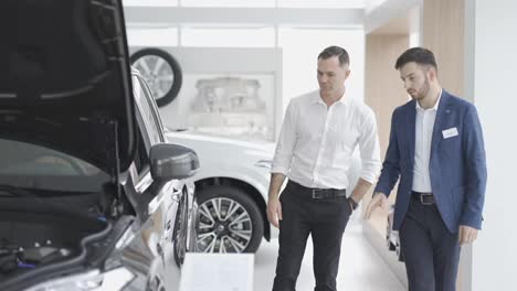 A-male-client-examine-car-at-dealership-with-the-help-of-auto-seller