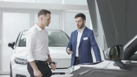Agent-talking-to-a-client-standing-near-open-hood-of-a-car