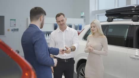 Young-married-couple-take-congratulations-from-auto-dealer,-hugging-each-other