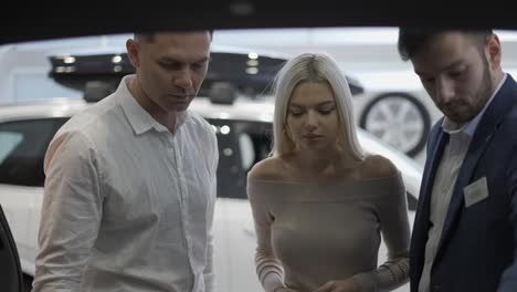 Car-agent-showing-trunk-from-inside-to-customers-in-automotive-dealership-showroom