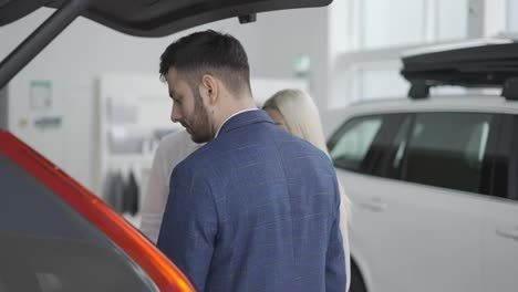 Salesman-showing-trunk-from-inside-to-customers-in-automotive-dealership-showroom