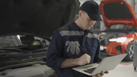 Car-mechanic-working-on-laptop-in-auto-repair-service,-lean-on-a-car