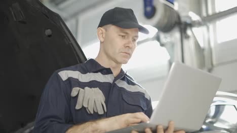 Car-mechanic-working-on-laptop-in-auto-repair-service,-low-angle-view