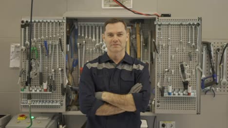 Porträt-Eines-Kfz-Mechanikers-In-Einer-Kfz-Werkstatt-In-Uniform-Mit-Ausrüstung-Im-Hintergrund