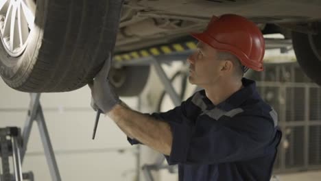 Auto-mechanic-working-underneath-car-lifting-machine-at-the-garage