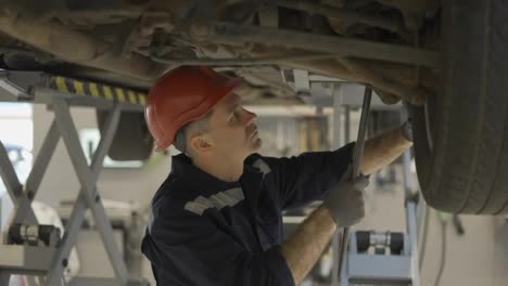 Auto-mechanic-in-helmet-working-underneath-car-lifting-machine-at-the-garage