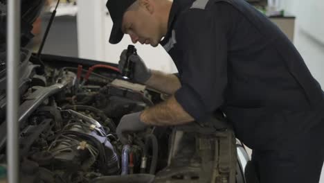 Car-service-worker-examining-engine-under-hood-with-flashlighter-in-hand
