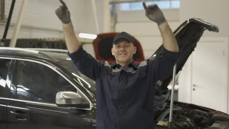 Smiling-mechanic-man-in-uniform-and-gloves-dancing-funny-in-a-modern-service-auto-center