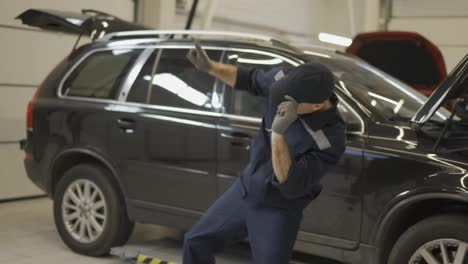 Happy-mechanic-man-in-uniform-and-gloves-dancing-funny-in-a-modern-service-auto-center