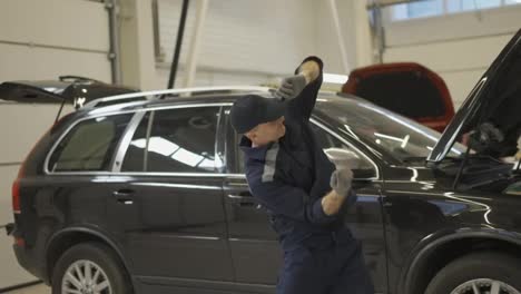 Happy-mechanic-man-dancing-funny-in-a-modern-service-auto-center,-slow-motion