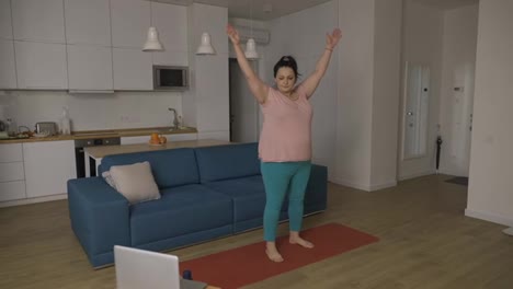 Plump-woman-performing-yoga-asana-at-home-with-online-tutor-on-laptop