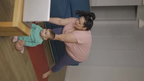 Overweight-woman-performing-yoga-asana-warrior-at-home-with-her-baby-on-the-floor