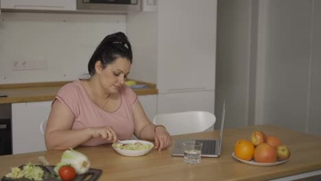 Overweight-woman-with-salad-in-front-of-laptop,-shows-disgust