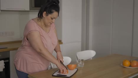 Attractive-overweight-woman-preparing-healthy-meal,-cutting-grapefruit