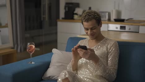Relaxful-homosexual-guy-in-fancy-dress-on-a-couch-using-mobile-phone