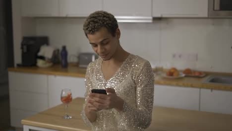 Cheerful-guy-in-fancy-dress-using-mobile-phone-at-home-kitchen