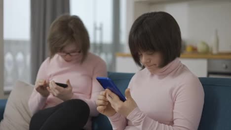 Two-girls-with-down-syndrome-are-holding-smartphones--looking-at-photos,-use-a-social-media-app