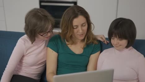 Mother-with-two-daughters-down-syndrome-sitting-on-sofa-have-fun-using-laptop
