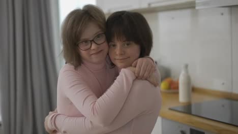 Zwei-Süße-Mädchen-Mit-Down-Syndrom-Stehen-Zusammen-Und-Umarmen-Sich-Zu-Hause