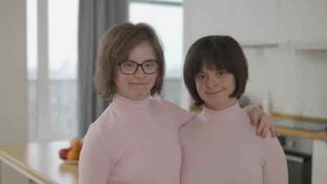 Portrait-of-two-cute-girls-with-down-syndrome-standing-together-embracing-at-home
