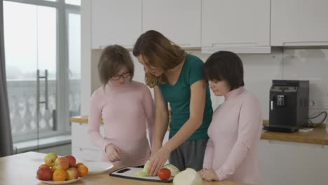 Two-girls-with-Down-Syndrome-are-learning-to-cook-with-their-mother-in-kitchen-at-home-with-fun-and-smile