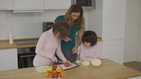 Two-girls-with-Down-Syndrome-cutting-vegetables-with-their-mother-in-kitchen-at-home