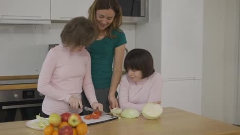 Two-girls-with-Down-Syndrome-cutting-vegetables-with-their-mother-in-kitchen