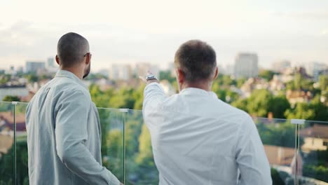 Two-happy-businessmen-chatting-on-a-terrace-overlooking-the-city.-Beautiful-view.-communication