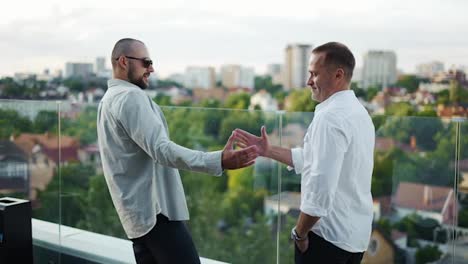 Two-happy-businessmen-meet-on-the-terrace-overlooking-the-city-and-shake-hands