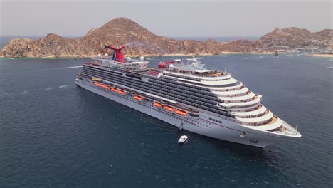 A-drone-circles-Carnival-Panorama-cruise-ship-anchored-in-the-bay-of-Cabo-San-Lucas,-Mexico