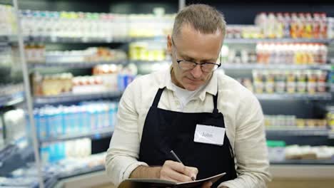 Portrait-of-a-sales-assistant-in-glasses-with-a-notebook-and-a-pencil-in-his-hands-in-a-grocery-store.-The-concept-of-work-in