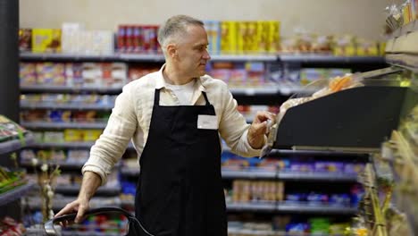 A-middle-aged-worker-in-a-grocery-store-puts-goods-on-the-shelves.-Working-with-bakery-products-in-the-store.-Control-of-goods-on-the-shelves