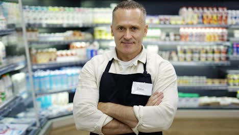 Portrait-of-a-middle-aged-shot-worker-in-and-apron.-The-man-puts-his-hands-on-his-chest.-The-concept-of-working-in-a-grocery
