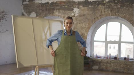 Portrait-smiling-woman-wearing-apron-to-start-painting-in-workshop