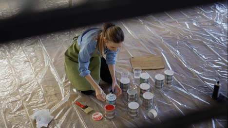 Woman-in-studio-workshop-open-different-colors-of-paint-in-metal-jars-on-the-floor
