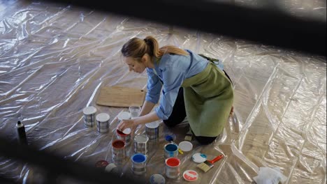 Woman-in-studio-open-different-colors-of-paint-in-metal-jars-on-the-floor-in-slow-motion