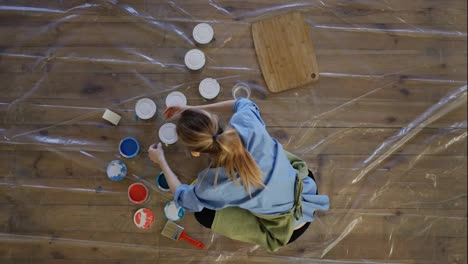 Woman-in-studio-open-different-colors-of-paint-in-metal-jars-on-the-floor,-view-from-above