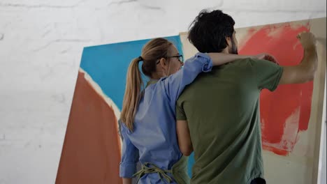Young-couple-paints-on-canvas-drawing-picture-in-art-studio,-woman-kiss-a-man