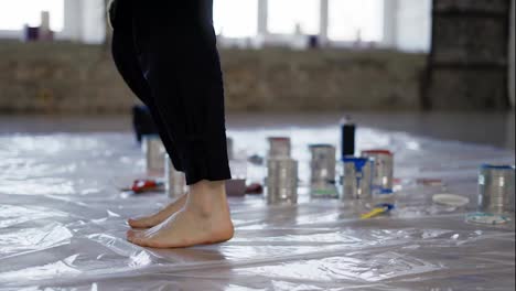 View-of-paint-cans-on-floor,-female-feet-she-dances-on-oilcloth