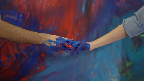 Couple-hands-in-paints-in-front-colorful-canvas,-touching-motion
