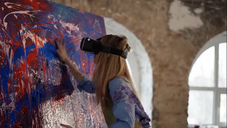 Woman-in-VR-mask-smear-the-paints-on-abstract-picture-on-easel