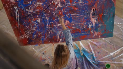 Woman-uses-brush-and-black-paints-splashing-gesture-on-canvas,-footage-from-above