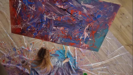 Woman-paints-on-canvas-dipping-hands-in-paints-jar,-footage-from-above
