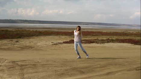 Young-woman-is-dancing-alone-standing-on-sand-beach-with-lake-line-on-background